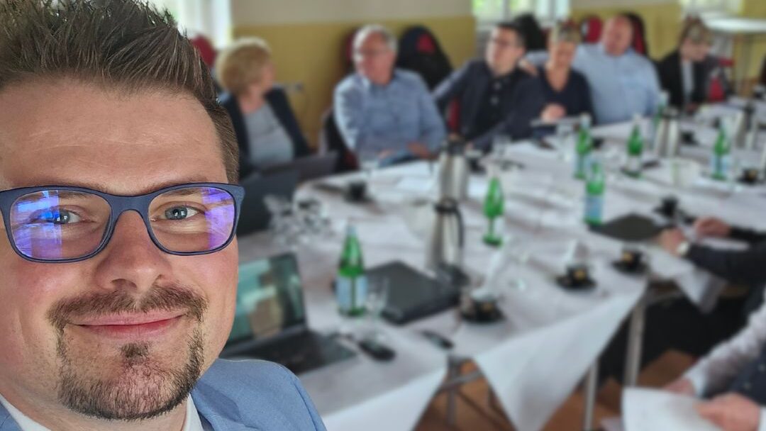 Tobias Kalski Wüstenrot Bausparkassen bei einem Seminar Vertriebsdirektor im hintergrund ist ein Tisch mit Wasserflaschen und anderen Menschen die unscharf sind